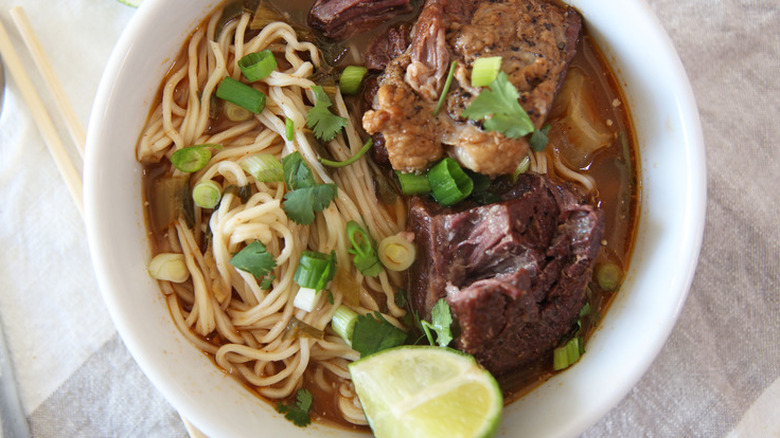 Bowl with noodles, sliced beef, lime wedge, and herbs. 