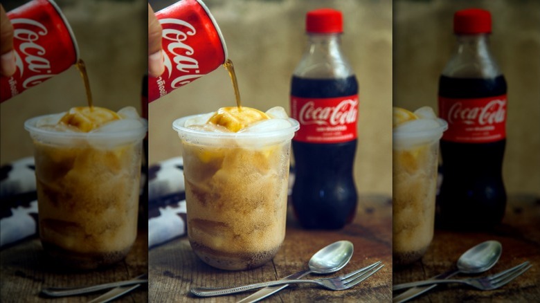 Coca-cola being poured into a cup with ice cream and ice, served with spoons and a soda