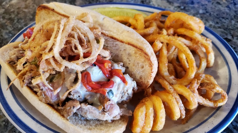 Slow-roasted pulled pork hoagie with diced green chiles, hatch cheese sauce, roasted red peppers, and topped with fried onion slivers. Served with curly fries.
