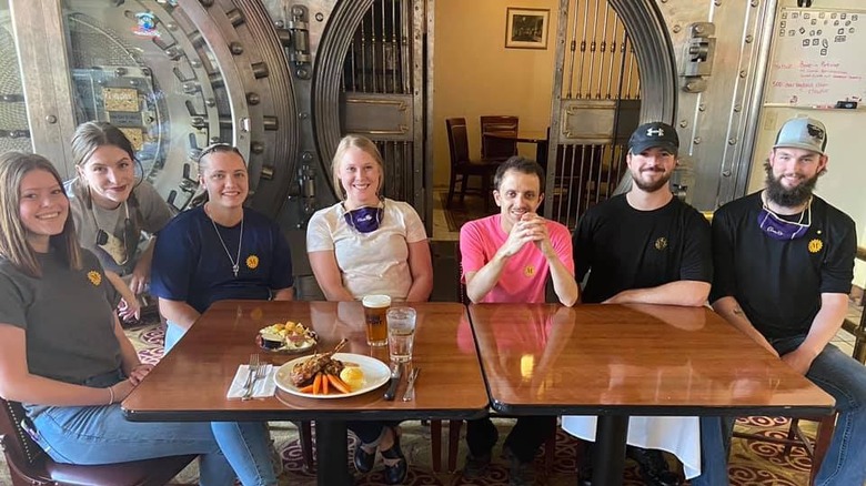 Customers sitting at a table with a plate of food on top and the original bank fault in the background