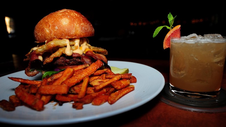 Hamburger and french fries on a plate next to a cocktail 