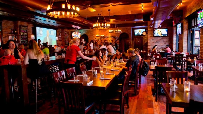 Dimly lit bar with exposed brick walls and people sitting and socializing at wooden tables. 