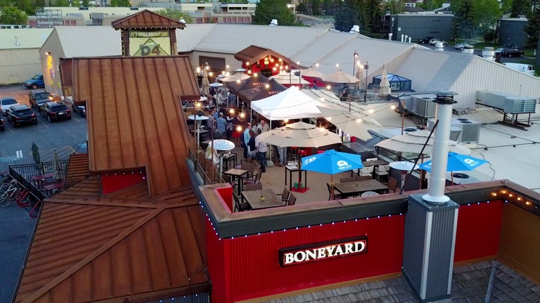 Aerial shot of a rooftop patio decorated with picnic tables, tents, and twinkle lights. There's a sign that says, "Boneyard" on the side of the building. 