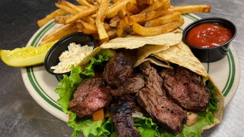 Beef wrap on a plate with a side of French fries. 