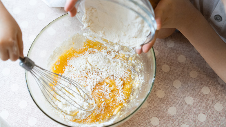 Person whisking flour and eggs in glass bowl