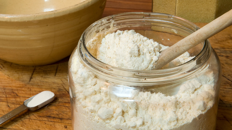 White flour in a glass jar with wooden spoon