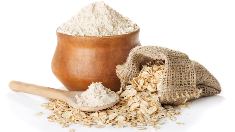 Oat flour in spoon next to burlap sack with oats