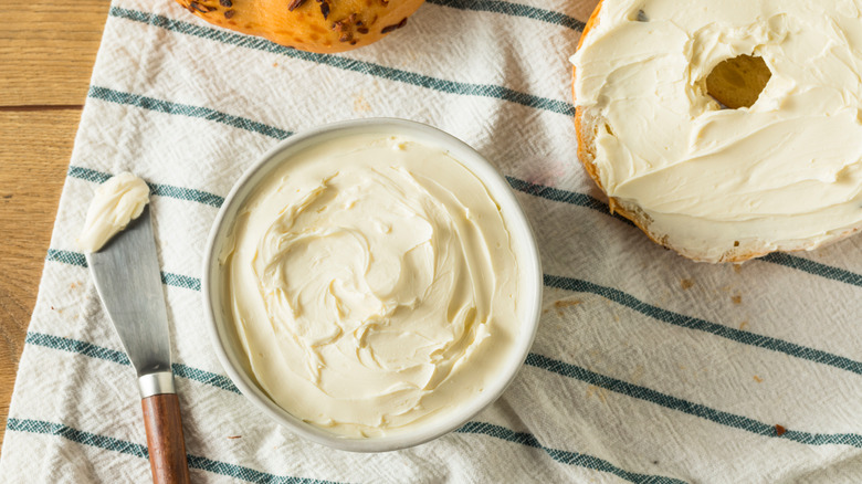 Tub of cream cheese on striped towel with spreading knife