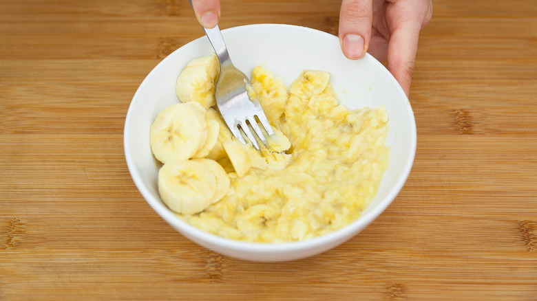 Bananas being mashed with fork in white bowl