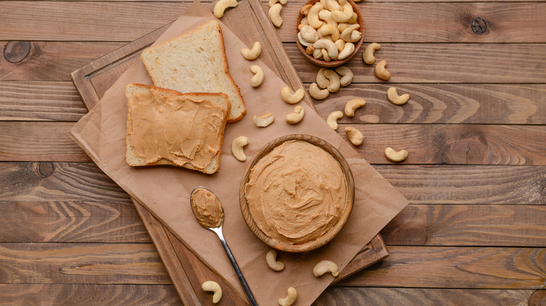 Cashew butter on wood table next to raw cashews