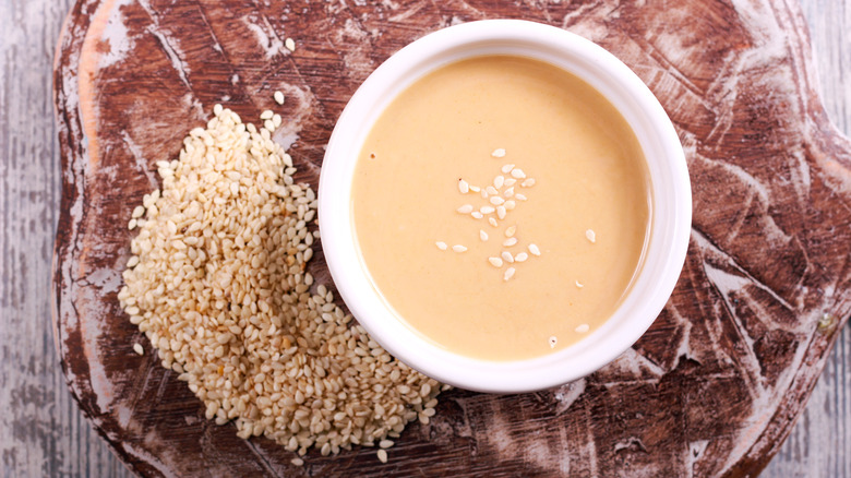 Sesame butter next to raw seeds on wood slab