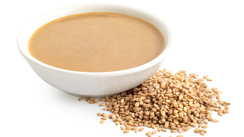 Tahini sauce in white bowl next to sesame seeds