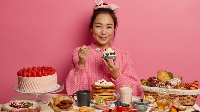 Woman holding dessert in front of table covered with desserts