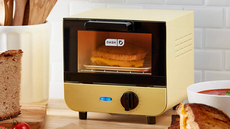 A Dash mini toaster on a wood countertop with a grilled cheese inside