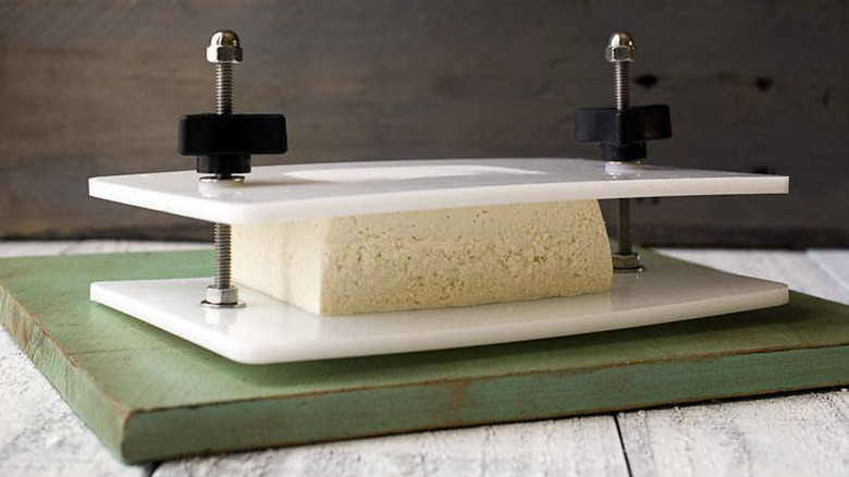 Tofu inside press on wooden board