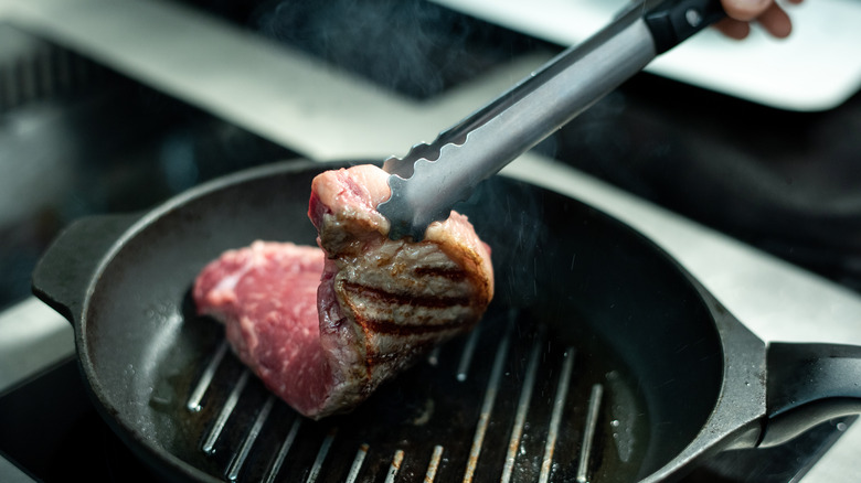 Stainless steel tongs flipping steak