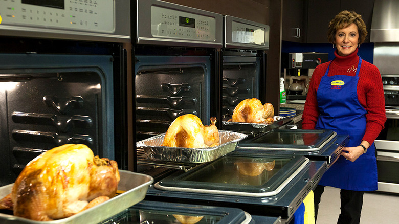 A female chef next to open ovens with turkeys