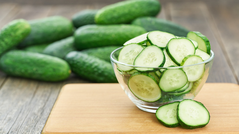 Sliced fresh cucumbers in a bowl with whole cucumbers in background.