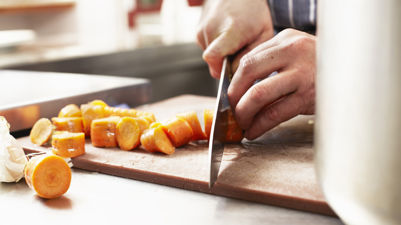 Person chopping carrots on board