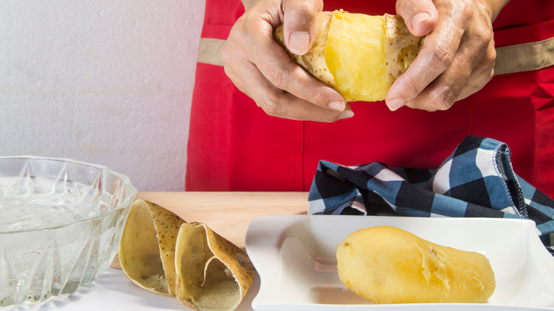 Person peeling boiled whole potatoes