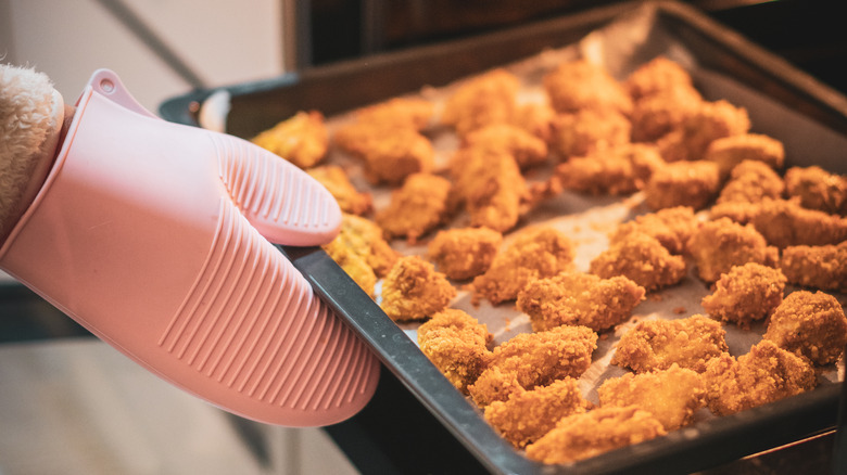 gloved hand putting nuggets in oven