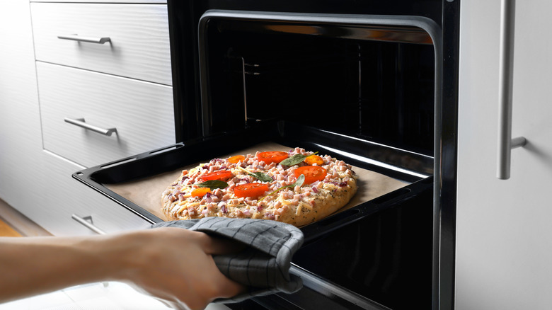 Woman taking pizza out of an oven