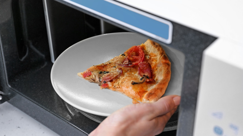 Woman putting a plate of pizza in a microwave