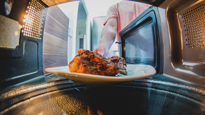 Man Taking a Cooked Chicken out of a Microwave