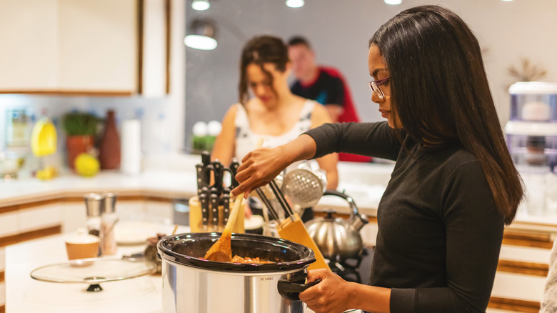 A young woman stirring food in a slow cooker.