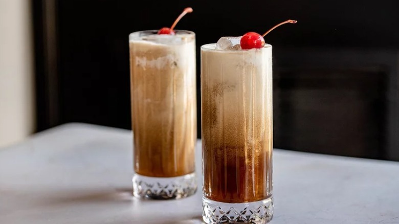 Two Colorado bulldog cocktails in tall glasses with maraschino cherries on white counter