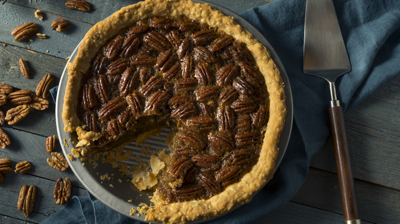 pecan pie in dish with loose pecans and serving utensil