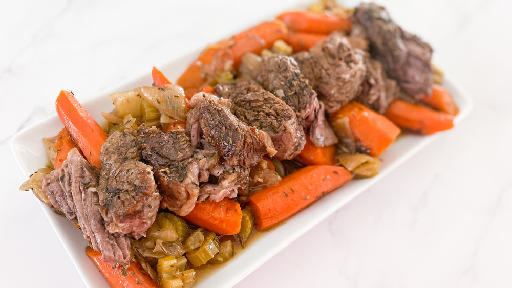 roast beef on white plate with carrots, onion, and celery