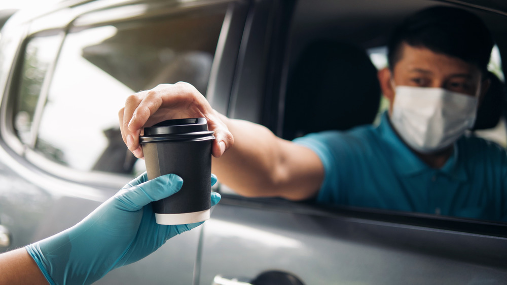 A hand handing a cup to a masked man in a vision of our dystopian present that will now be marketed as our high tech utopian future.