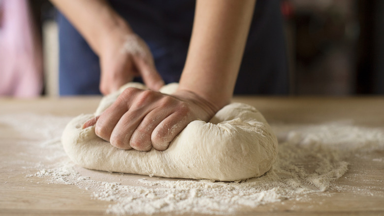 Hands kneading pizza dough on floured surface