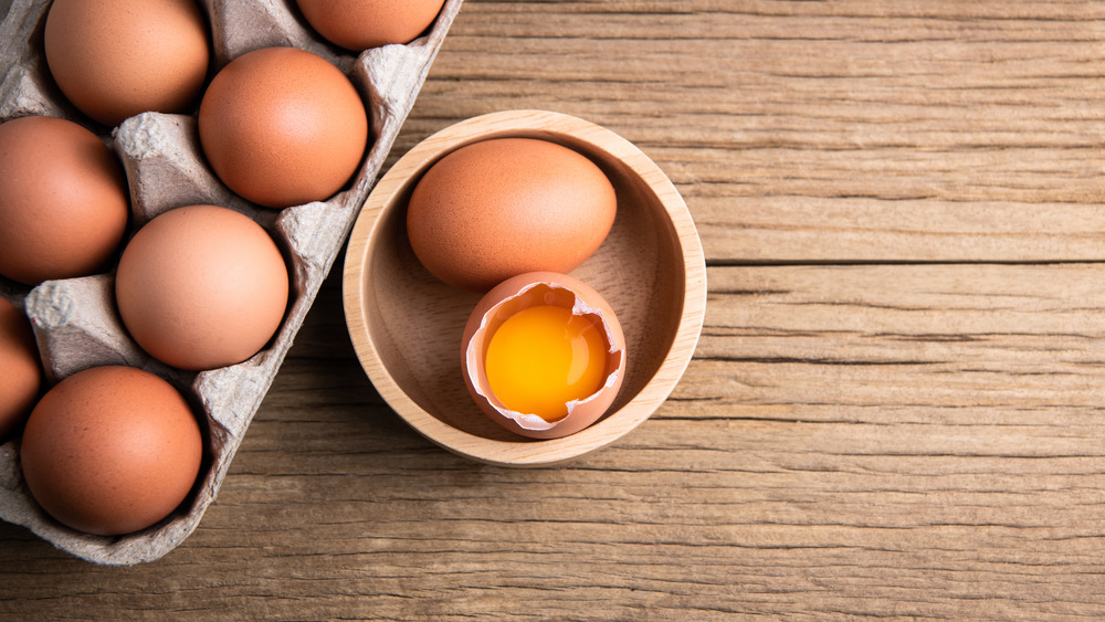 a dozen eggs with one egg cracked open in a bowl