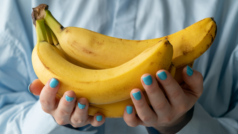 Hands with blue nails holding bunch of bananas