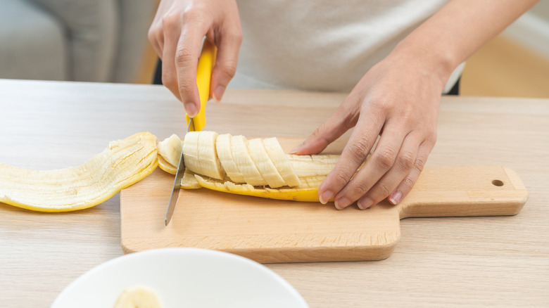 Woman slicing banana on wooden cutting board