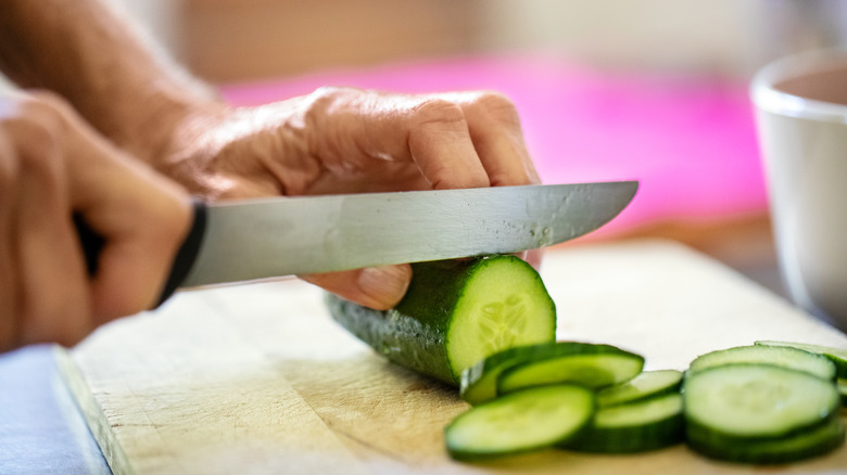 person chopping cucumber on cutting board