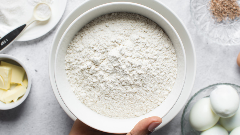 Hand holding white bowl full of flour