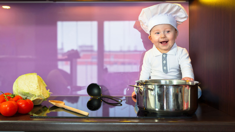 Baby chef in hat working with pot in kitchen