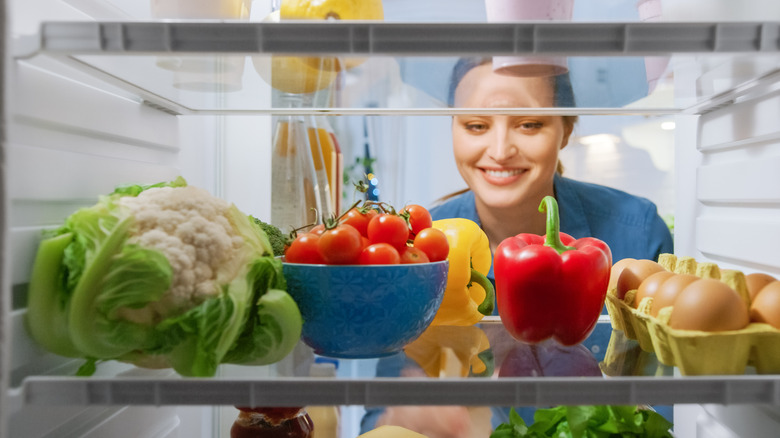 Lady looks into refrigerator full of unwrapped food