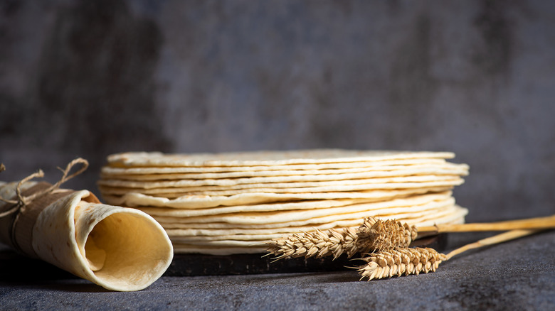 stack of flour tortillas and wheat with gray background