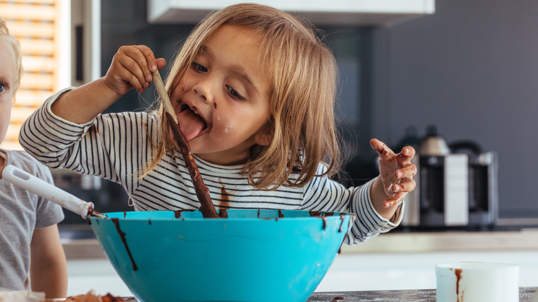 Little girl licking bowl of muffin batter