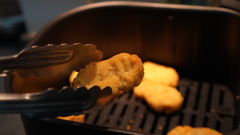 Nugget held with tongs next to the air fryer