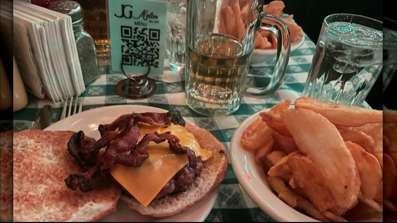 JG Melon Burger with bacon and cheese and fries on a table