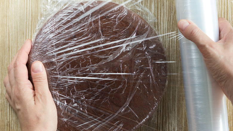 Chocolate cake being wrapped in platic wrap