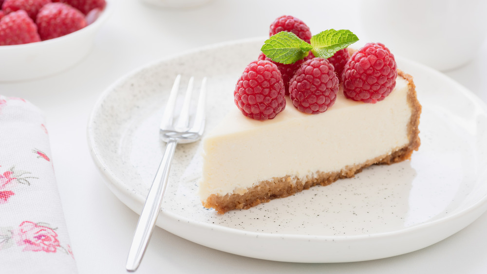 Round cheesecake cut into slices topped by strawberries