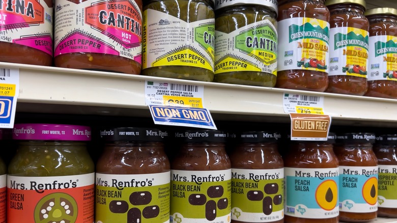 Different salsa brands in jars on grocery shelf.