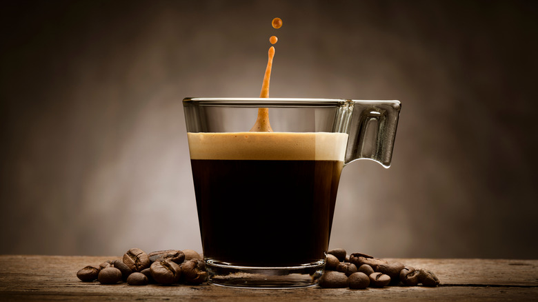 coffee in glass mug next to pile of beans