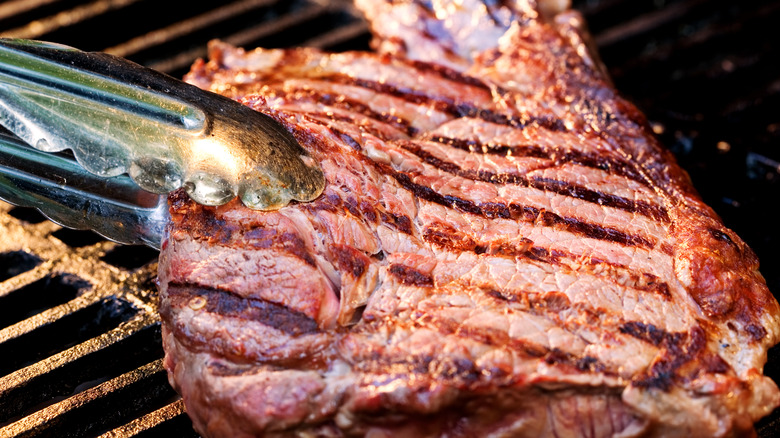 Sirloin steak on barbecue grill with tongs